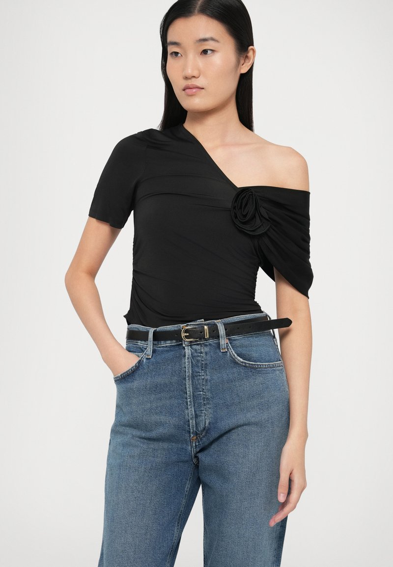 Zwarte een-schouder top gemaakt van gladde stof, met een geraffineerde textuur en een bloemaccent. Gecombineerd met high-waisted blauwe denim jeans.