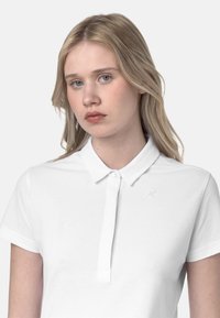 Polo bianca a maniche corte, con bottoni e un logo discreto sul petto. Tessuto liscio e design classico.