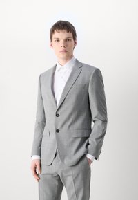 Completo grigio su misura con motivo a quadri, giacca monopetto con revers, due tasche frontali, abbinato a una camicia bianca.