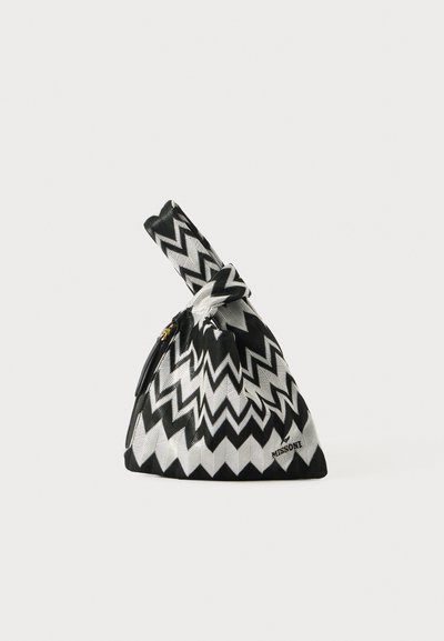Sac en tissu à motif zigzag noir et blanc de forme triangulaire, noué en haut, avec une fermeture éclair dorée et une étiquette de marque.