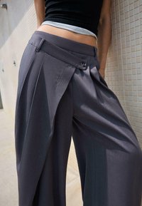 Weitbeinige graue Hosen mit einem gepolsterten Design, ausgestattet mit einem Knopfverschluss und einem glatten, strukturierten Stoff.