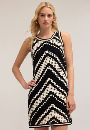 Vestido de ganchillo en blanco y negro con un patrón en zigzag, diseño sin mangas, cuello redondo y tejido texturizado.