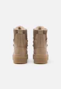 Τα ταμπά μποτάκια με τονίστη πλευρά διαθέτουν σουέτ πάνω μέρος, χνουδωτή επένδυση και χοντρή ελαστική σόλα με κάθετους αυλακώματος. Σχέδιο με κορδόνια και πλαϊνές λεπτομέρειες.