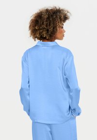 Camicia di satin blu chiaro con colletto, maniche lunghe e vestibilità rilassata. Texture liscia con un leggero lucido. Vista posteriore mostrata.
