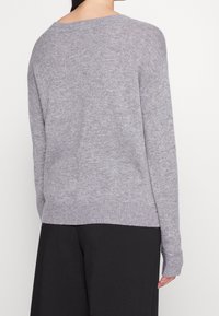 Pull en maille grise à coupe décontractée, col large et ourlet côtelé ; doté de manches longues avec des poignets légèrement lâches.