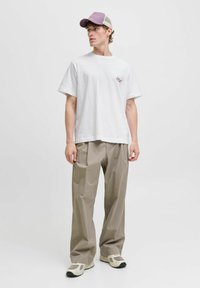 Hvid bomulds t-shirt med lille broderet design, parret med beige løse bukser og en lavendel mesh baseball cap. Neutrale fodtøj.