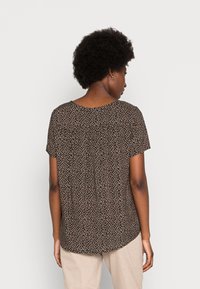 Top de manga curta, com padrão floral castanho, com decote arredondado e bainha curva. O material parece leve, com uma textura suave.