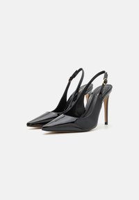 Musta kiiltonahkakengät, joissa on terävät varpaat, korkeat stiletto-korkokengät ja nilkkahihnat, joissa on kultasävytteiset yksityiskohdat.