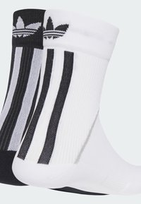 Two pairs of crew socks: one black with gray stripes and logo, one white with black stripes and logo. Ribbed texture, contrasting colors.