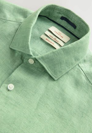 Polo shirt verde chiaro con tessuto testurizzato, colletto con bottoni e bottoni bianchi. Presenta etichette che indicano una vestibilità regolare, 100% lino.