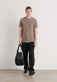 Brun polo skjorte med korte ærmer og krave, kombinert med sorte bukser og bæret en svart bag. Glatt stoff og skreddersydd passform.