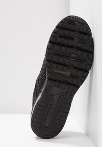 Podeszwa czarnego buta sportowego z teksturowaną powierzchnią gumową, wyróżniająca się wyraźnym bieżnikiem i widocznym logo.