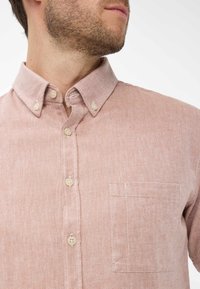 Camicetta rosa a maniche corte con bottoni, realizzata in tessuto texturizzato, colletto standard, taschino anteriore e bottoni beige. Motivo a spina di pesce visibile.