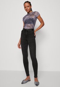 Grå tie-dye t-skjorte med kort erm, høytlivs svarte skinny jeans og grå slip-on sko med dekorative metalldetaljer.