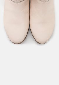 Botines de cuero rosa claro con punta redonda, textura sutil y un tacón bajo y suave. Sin patrones visibles ni detalles metálicos.
