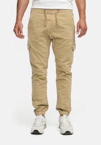 Pantalones cargo beige con cintura elástica y cordón, que cuentan con bolsillos laterales y puños ajustados, fabricados en material de algodón.