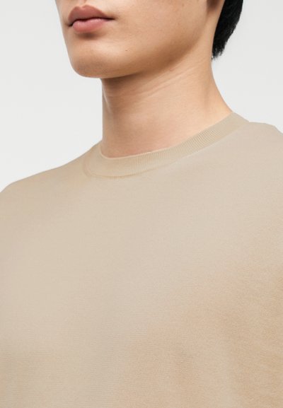 Μπεζ πουλόβερ με στρογγυλή λαιμόκοψη, απαλό ύφασμα και ριμπ λεπτομέρειες στη λαιμόκοψη, με εφαρμοστή σιλουέτα και ελάχιστες ραφές.