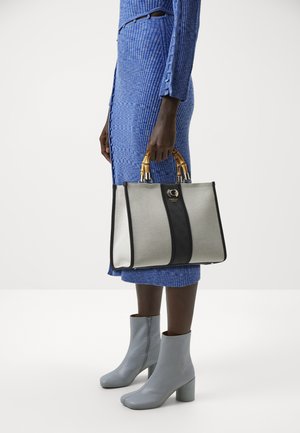 Silver handbag with black accents and patterned texture. Features dual bamboo handles and a logo detail on the front.