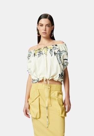 Top bianco off-the-shoulder con stampa floreale, orlo arricciato, abbinato a una gonna gialla con tasche cargo e vita elasticizzata.