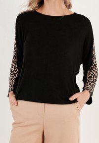Černý top s dlouhými rukávy s leopardím potiskem na rukávech. Měkký materiál s volným střihem a kulatým výstřihem.