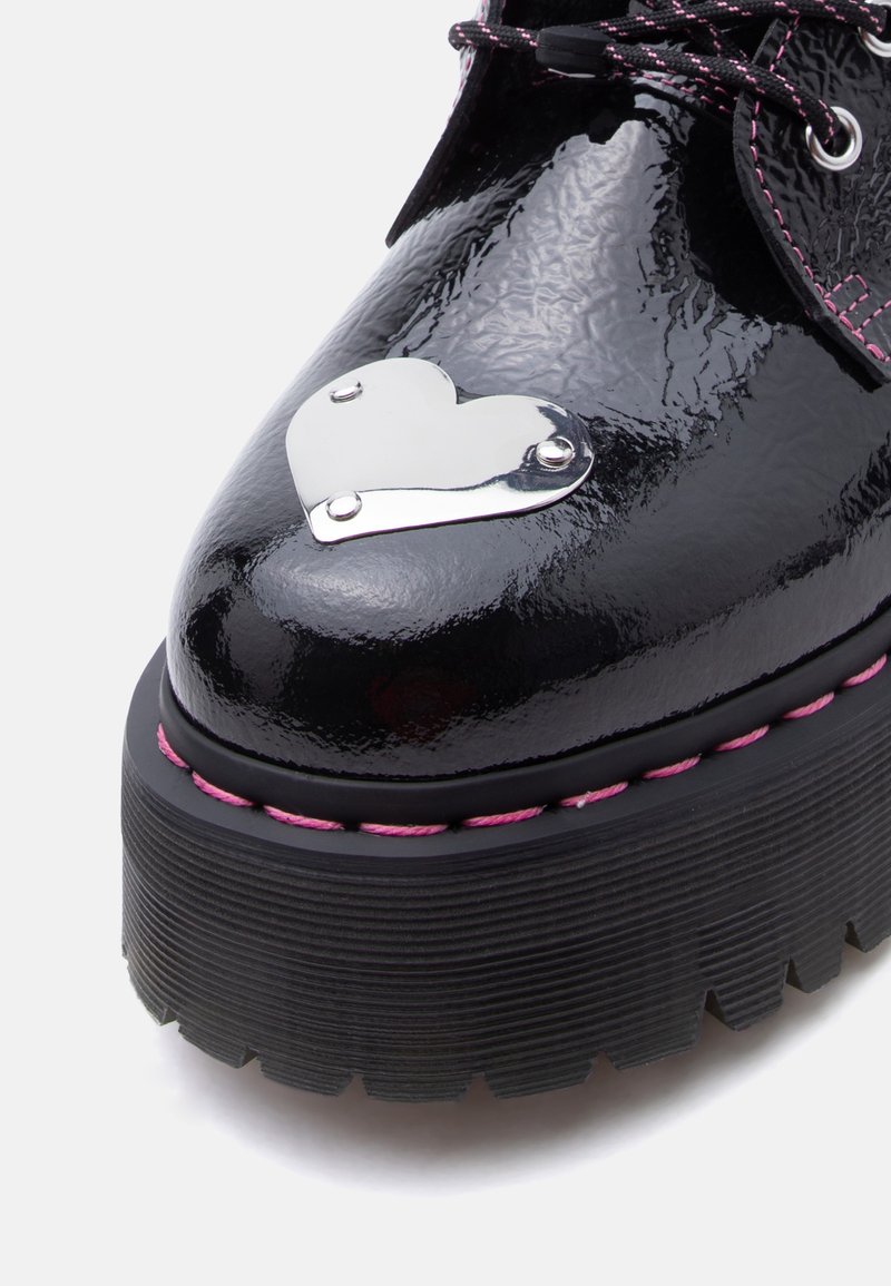 Zwart lakleren plateau schoen met dikke zool, roze stiksels, veters met roze accenten en een zilveren metalen hart bevestigd aan de neus.
