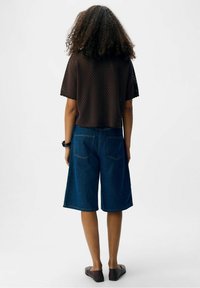 Haut marron en maille à manches courtes avec motif en maille, associé à un short en denim bleu longueur genou avec poches arrière et coupe décontractée.