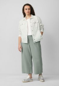 Witte denimjas, wit T-shirt, lichtgroene wijde broek en zilveren sneakers. Opvallende details zijn de knoopzakken en de losse pasvorm.