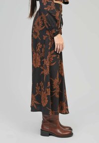 Jupe longue noire avec un motif floral rouille, fabriquée en tissu doux. Associée à des bottines en cuir marron et un haut ajusté.