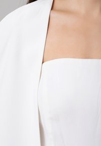 Top blanc sans bretelles avec une texture lisse et mate, présentant un corsage ajusté et un sur-étage en chiffon doux et drapé.