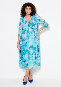 Blommig omlottklänning i blå nyanser med trekvartslånga ärmar och midja som är insnörd. Kombinerad med blå högklackade skor med spetsiga tår.