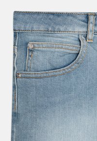 Jeans de denim azul claro con un ligero desgastado, que cuentan con un bolsillo frontal, costura de cobre y remaches metálicos. Textura suave y diseño clásico.