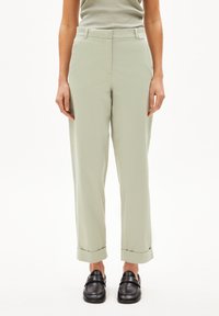 Hellgrüne, hoch taillierte Hose mit geradem Schnitt, umgeschlagenen Säumen und glatter Textur. Kombiniert mit schwarzen Slippern.