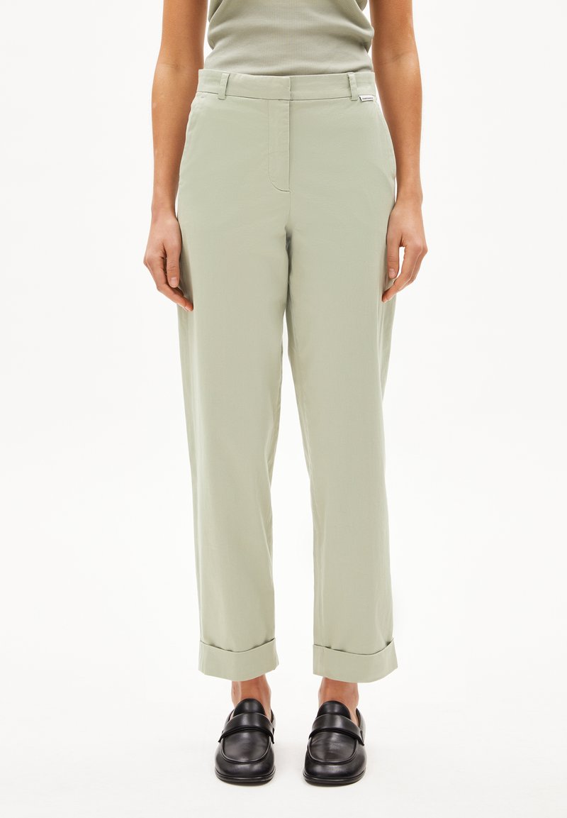 Hellgrüne, hoch taillierte Hose mit geradem Schnitt, umgeschlagenen Säumen und glatter Textur. Kombiniert mit schwarzen Slippern.