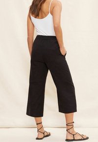 Czarne spodnie 3/4 z elastycznym pasem, prostym krojem i bocznymi kieszeniami, w zestawie z czarnymi sandałami na cienkich paskach. Gładka struktura materiału.