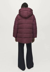 Vínová prošívaná bunda s kapucí, volného střihu, v kombinaci se širokými tmavými kalhotami.