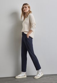 Beige gebreide trui, marineblauwe gestreepte broek en witte sneakers met beige accenten. De outfit heeft een losse pasvorm en subtiele texturen.