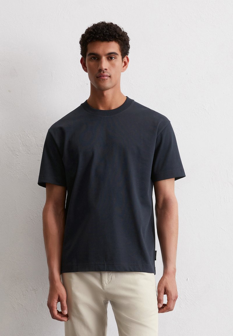 Granatowa bawełniana koszulka z krótkim rękawem, okrągłym dekoltem i prostym dołem. Posiada subtelną teksturę i małą metkę po boku.