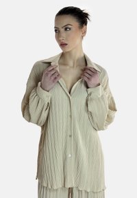 Chemise boutonnee de couleur crème, texturée, avec un motif de feuilles, dotée d'un col et de manches légèrement volumineuses.