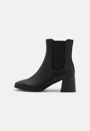 Černá kotníková bota s hladkým koženým povrchem, elastickými bočními panely a robustním hranatým podpatkem. Má špičatý design špičky.