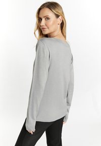 Maglione grigio a maglia con maniche lunghe, scollatura a V e vestibilità leggermente morbida. Indossato con pantaloni neri. Texture soffice e design semplice.