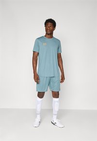 T-shirt de sport bleu clair et shorts en tissu évacuant l'humidité. Présente un logo orange, des chaussettes blanches hauteur genou et des chaussures de sport blanches.