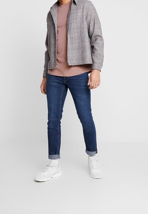 Chemise à carreaux gris et blanc, portée sur un t-shirt rose poussiére. Jean bleu ajusté avec les revers roulés et baskets blanches complètent la tenue.