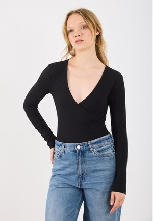 Svart ribbet bodysuit med lange ermer og dyp V-hals, kombinert med lyseblå høydeisede jeans. Enkelt og tettsittende silhuett.