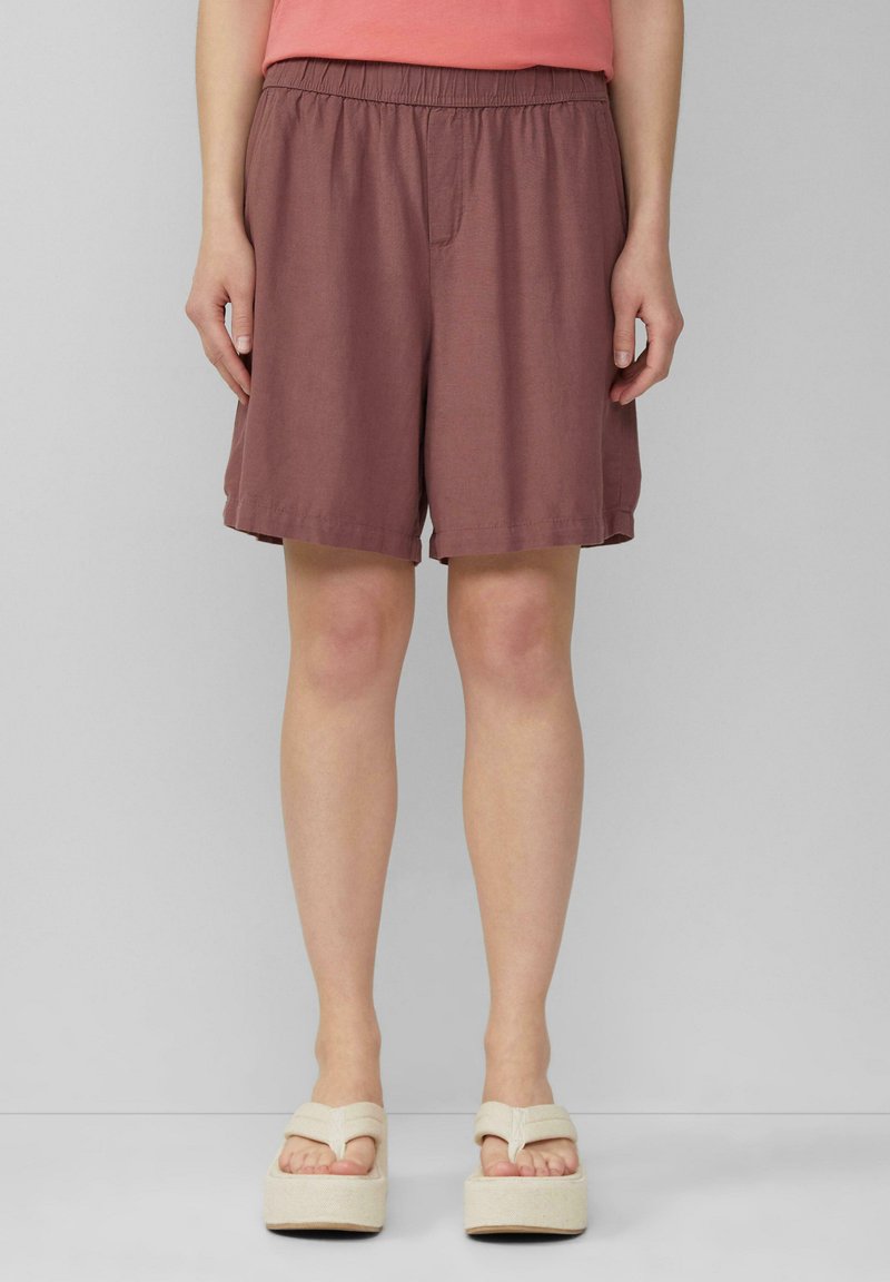 Burgunderfarbene Shorts mit einem elastischen Bund, knielang, aus leichtem Stoff. Kombiniert mit beigen Plateausandalen mit einem Überkreuzriemen.