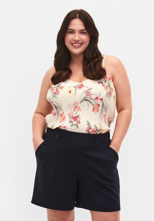 Camisole crème à motif floral avec des bretelles fines, associé à un short taille haute bleu marine avec des poches latérales et deux boutons à la taille.
