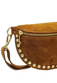 Pochette en daim marron avec une forme arrondie, quincaillerie dorée, fermeture éclair et clous décoratifs dorés le long du bord.