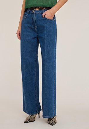 Jeans de mezclilla azul de pierna ancha con una cintura de media altura, que cuentan con dos bolsillos frontales y un cierre de un solo botón, combinados con zapatos de tacón alto texturizados.
