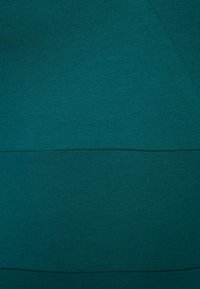 Turkoosi venyvä kangas, jossa on tasainen pinta, ja johon on ommeltu kaksi va horizontalista osaa erottavat kontrastiset ommelviivat. Yksinkertainen, minimalistinen muotoilu.
