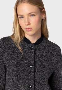 Giacca in misto lana di colore grigio scuro con leggere tracce chiare, caratterizzata da un colletto tondo, cinque bottoni neri e un design a maglia testurizzata.