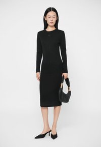 Black long-sleeve dress with a bodycon fit and ribbed texture, paired with a black handbag featuring a gold accent.